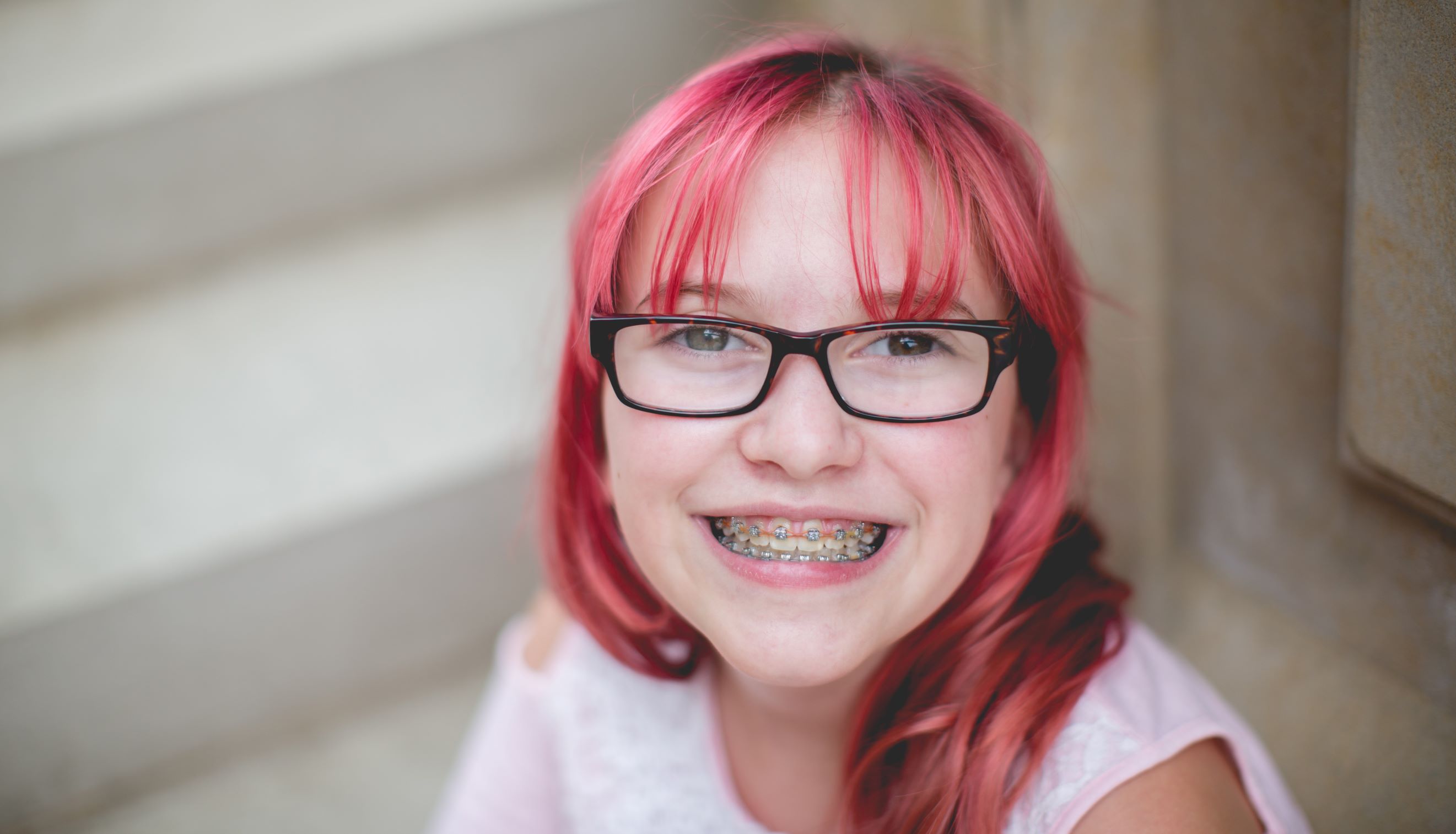 Girl with pink hair, glasses, and braces smiling at the camera